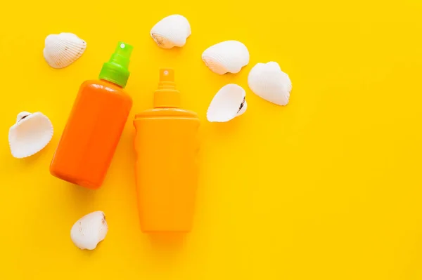 Top view of bottles of sunscreens near seashells on yellow background — Stock Photo