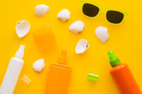 Muscheln in der Nähe von Sonnenschutzmitteln und Sonnenbrillen auf gelbem Hintergrund — Stockfoto