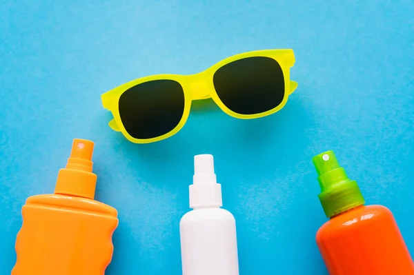 Top view of sunglasses near bottles of sunscreens on blue background — Stock Photo