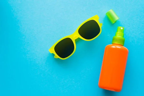 Вид сверху солнцезащитных очков рядом с бутылкой солнцезащитного крема на синем фоне — стоковое фото