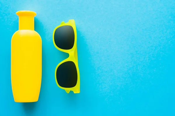 Top view of sunglasses and sunscreen on blue background with copy space — Stock Photo