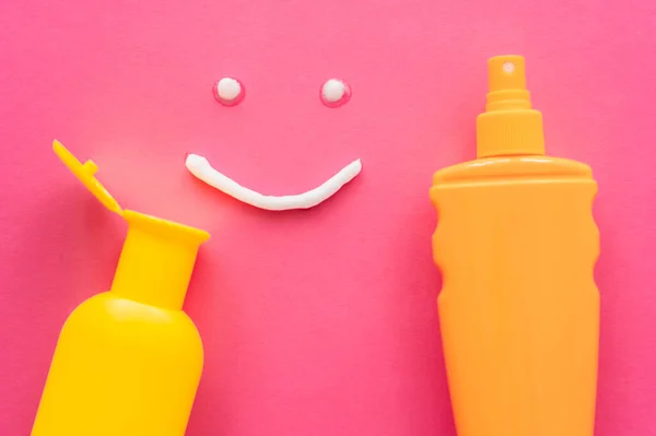 Vista superior del letrero de sonrisa cerca de botellas de protector solar sobre fondo rosa - foto de stock