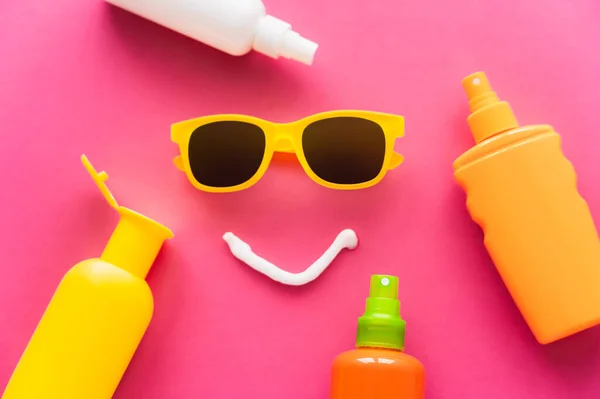 Вид зверху сонцезахисні окуляри біля пляшок сонцезахисних кремів на рожевому фоні — стокове фото
