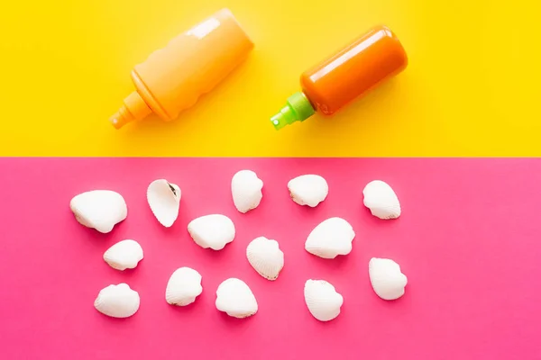 Top view of seashells near bottles of sunscreens on yellow and pink background — Stock Photo