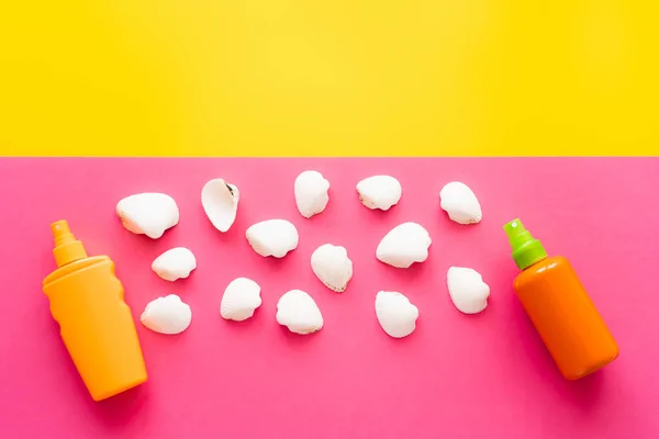 Top view of white seashells near sunscreens on yellow and pink background — Stock Photo