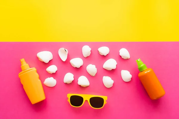 Muscheln in der Nähe von Sonnenbrillen und Sonnenschutzmitteln auf gelbem und rosa Hintergrund — Stockfoto