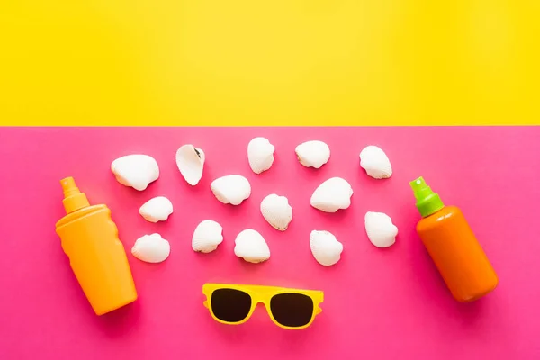 Vista dall'alto di conchiglie vicino occhiali da sole e creme solari su sfondo giallo e rosa — Foto stock