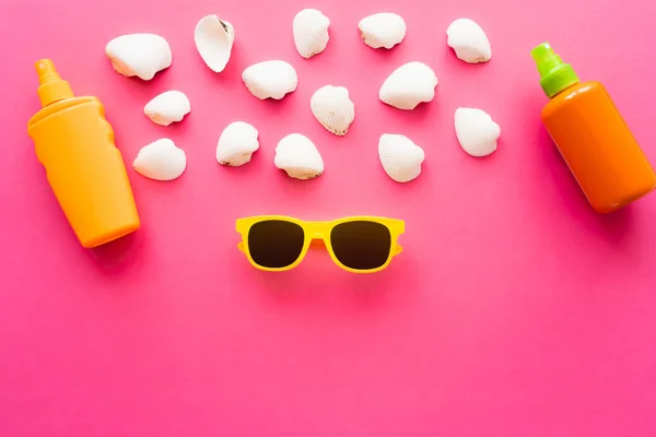 Vista superior de óculos de sol perto de conchas e protetores solares em fundo rosa — Fotografia de Stock