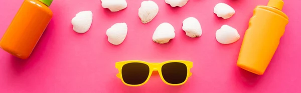 Vista superior de óculos de sol perto de conchas brancas e protetores solares em fundo rosa, banner — Fotografia de Stock