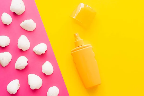 Top view of seashells and sunblock on pink and yellow background — Stock Photo