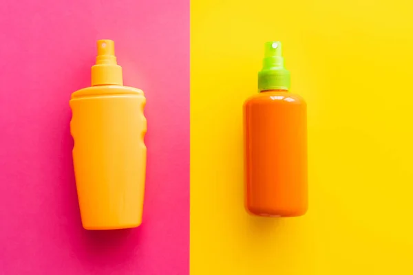 Top view of bottles of sunscreens on pink and yellow background — Stock Photo