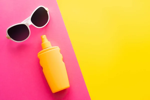 Top view of sunglasses and sunblock on pink and yellow background — Stock Photo