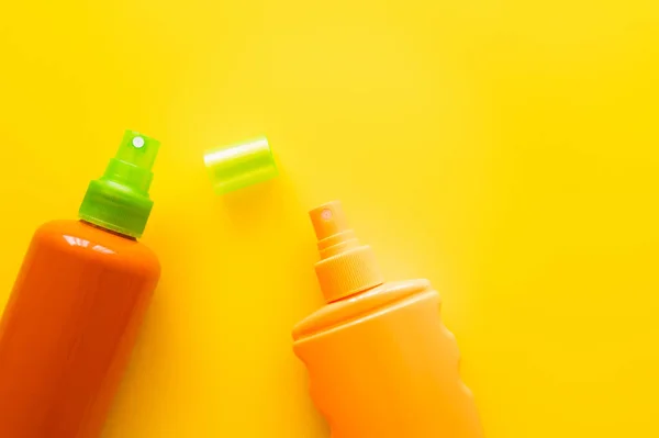 Vista superior de botellas de protectores solares en superficie amarilla - foto de stock
