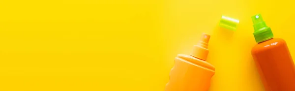 Top view of bottles of sunscreens near cap on yellow surface, banner — Stock Photo