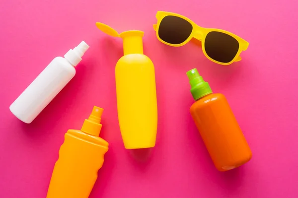 Vista superior de garrafas de protetores solares perto de óculos de sol na superfície rosa — Fotografia de Stock