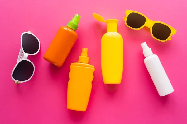 Верхний вид солнцезащитных очков и бутылок солнцезащитных кремов на розовой поверхности — стоковое фото