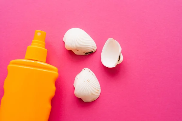 Draufsicht auf Muscheln und eine Flasche Sonnencreme auf rosa Oberfläche — Stockfoto