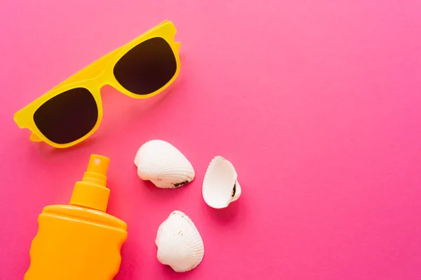 Vue de dessus des lunettes de soleil près de la crème solaire et des coquillages sur la surface rose — Photo de stock