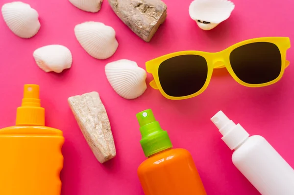 Top view of sunscreens near sunglasses and seashells on pink background — Stock Photo