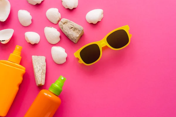 Vista dall'alto di occhiali da sole vicino a creme solari e conchiglie su sfondo rosa — Foto stock