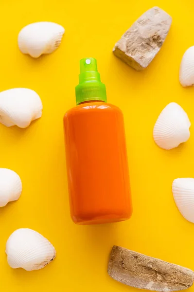 Top view of bottle of sunscreen near seashells and stones on yellow background — Stock Photo