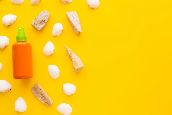 Top view of seashells and sunscreen in bottle on yellow background — Stock Photo