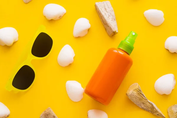 Top view of sunblock near seashells and sunglasses on yellow background — Stock Photo