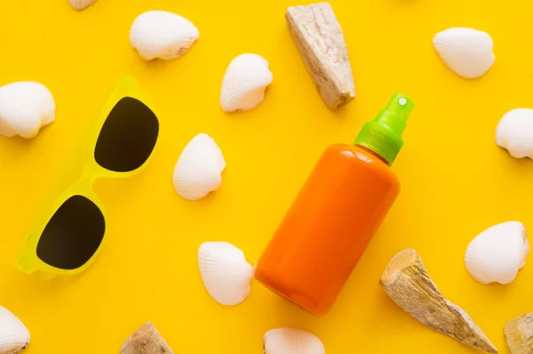 Vue de dessus de la crème solaire près des coquillages et des lunettes de soleil sur fond jaune — Photo de stock