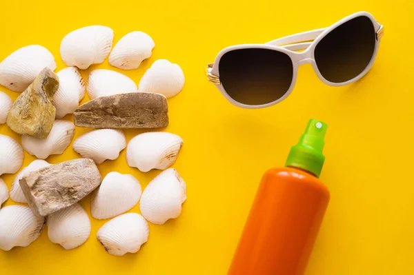 Top view of sunglasses near seashells and sunblock on yellow background — Stock Photo