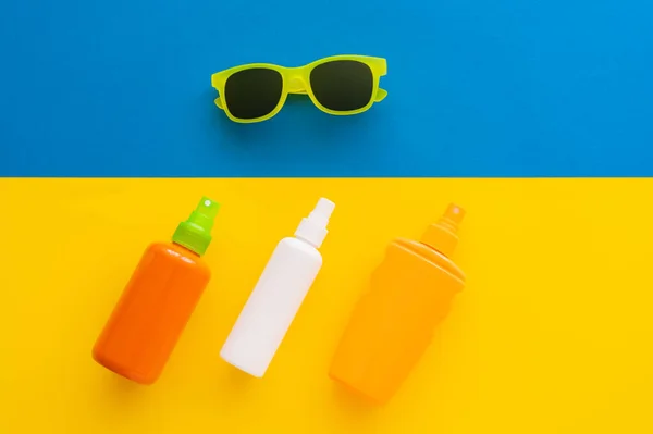 Vista dall'alto di creme solari e occhiali da sole su sfondo giallo e blu — Foto stock