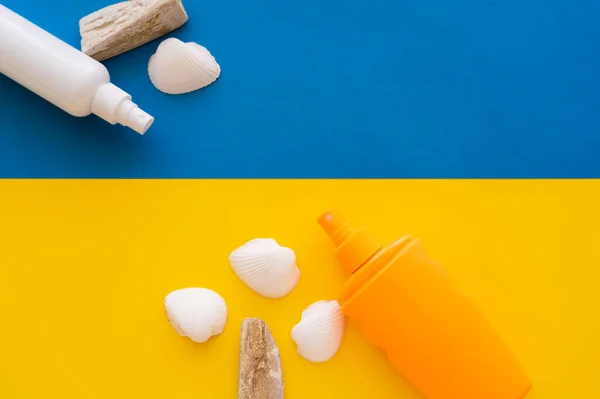 Vista dall'alto di creme solari vicino conchiglie e pietre su sfondo giallo e blu — Foto stock