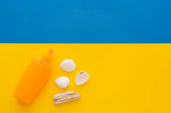 Top view of sunscreen near seashells on yellow and blue background — Stock Photo