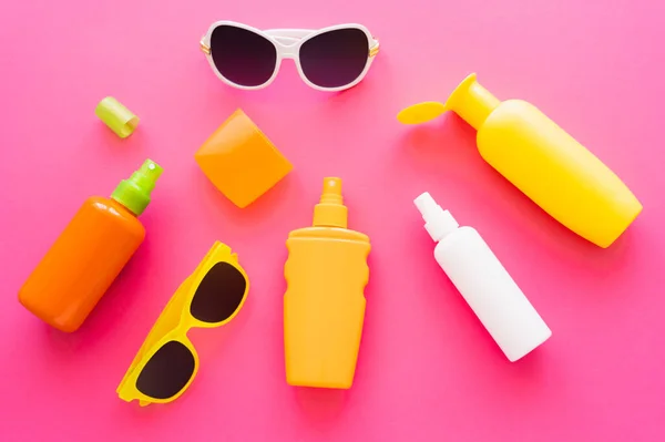 Vista dall'alto di creme solari con tappi e occhiali da sole sulla superficie rosa — Foto stock