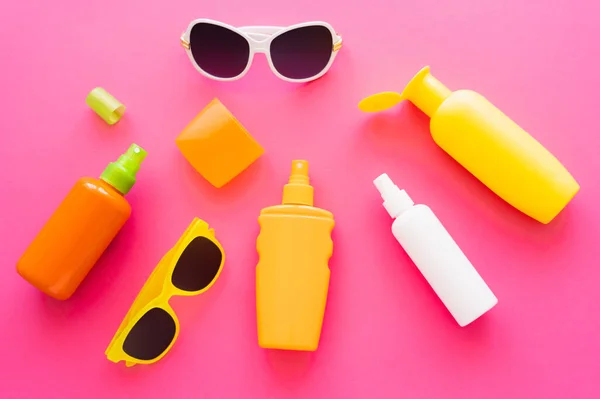 Top view of sunscreens with caps and sunglasses on pink surface — Stock Photo