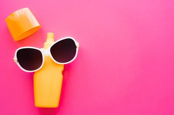 Vue de dessus des lunettes de soleil sur écran solaire sur surface rose — Photo de stock