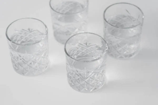 Vue grand angle de l'eau dans des verres avec motif à facettes sur la surface blanche — Photo de stock