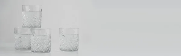 Faceted glasses with water on grey background with copy space, banner — Stock Photo