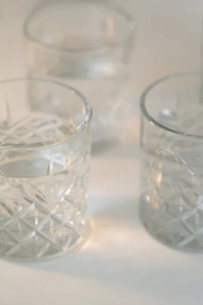 Close up view of faceted glasses with clean water on blurred grey background — Stock Photo