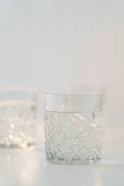 Glass with faceted pattern and pure water on grey blurred background — Stock Photo