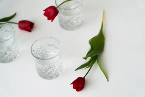 Hochwinkelaufnahme von verschwommenen Tulpen und Gläsern mit reinem Wasser auf weißer Tischplatte — Stockfoto