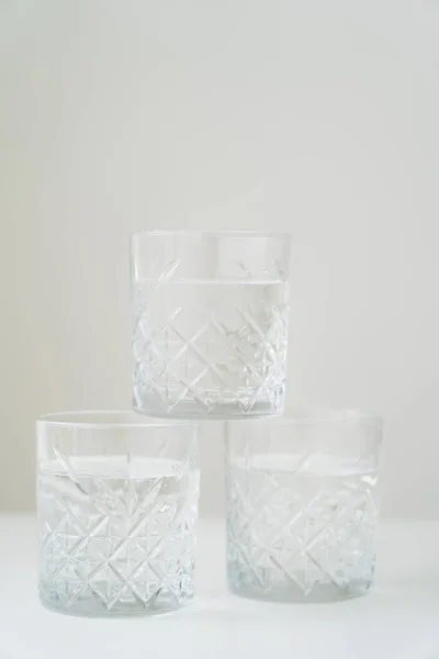 Pilha de copos de cristal com água pura na superfície branca isolada em cinza — Fotografia de Stock