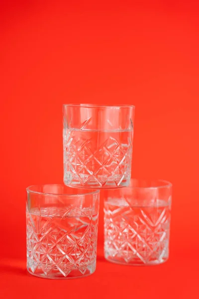 Verres en cristal avec de l'eau claire empilée sur fond rouge vif — Photo de stock