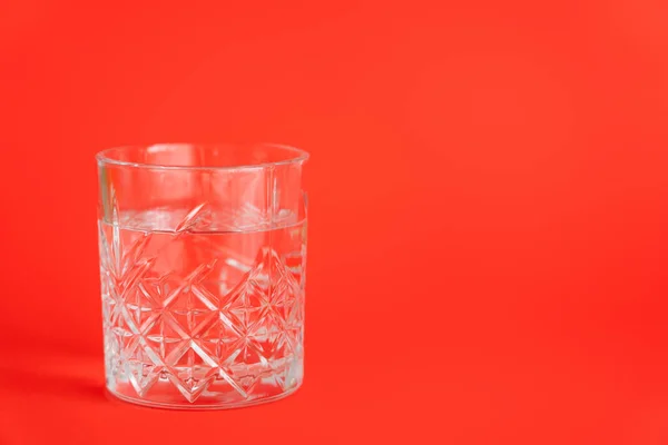 Faceted transparent glass with fresh water on red background with copy space — Stock Photo