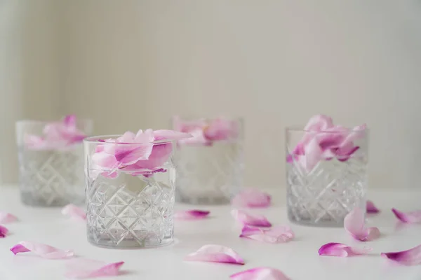 Copos de cristal com tônico e pétalas na superfície branca e fundo cinza borrado — Fotografia de Stock