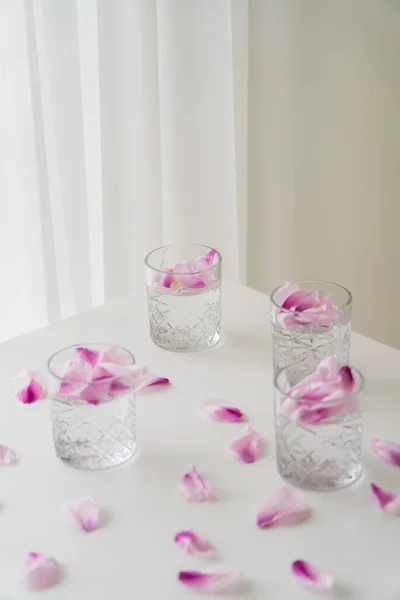 Vista en ángulo alto de las gafas con pétalos tónicos y florales sobre mesa blanca y fondo gris - foto de stock