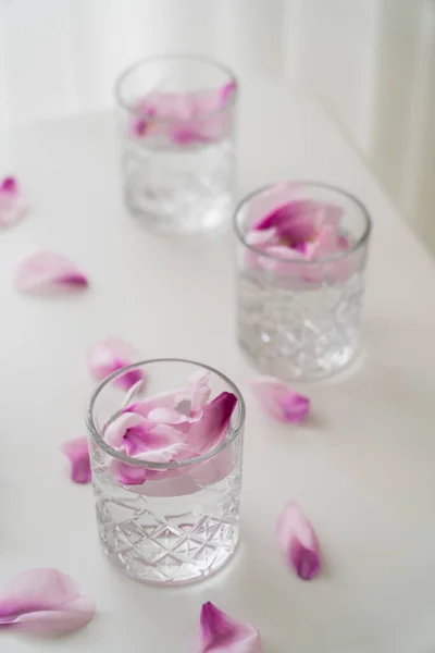 High angle view of faceted glasses with tonic and natural petals on white surface — Stock Photo