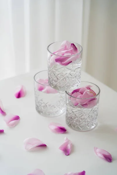 Copos de cristal com pétalas tônicas e florais em mesa branca e fundo cinza — Fotografia de Stock