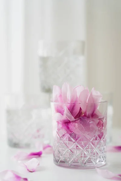 Close up view of transparent glass with tonic and petals on blurred grey background — Stock Photo