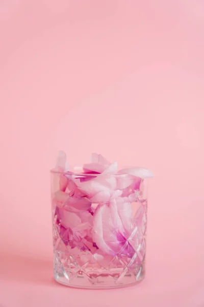 Vetro cristallo con petali floreali naturali e tonico su sfondo rosa — Foto stock