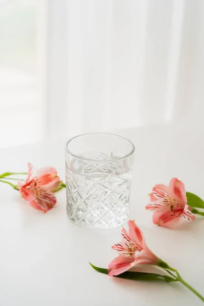 Verre transparent avec de l'eau douce près de fleurs alstroemeria rose sur fond blanc avec espace de copie — Photo de stock